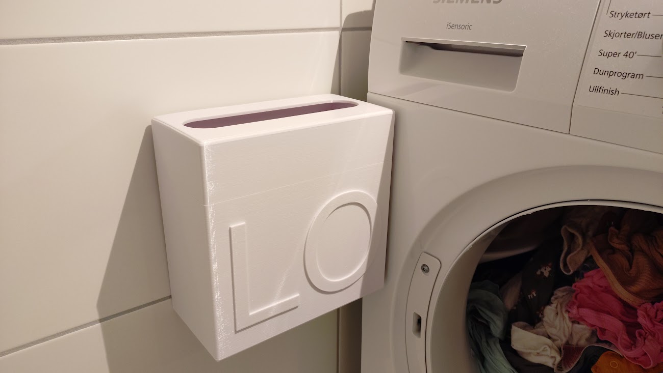 Picture of a white lint bin hanging on the wall next to a clothes dryer.